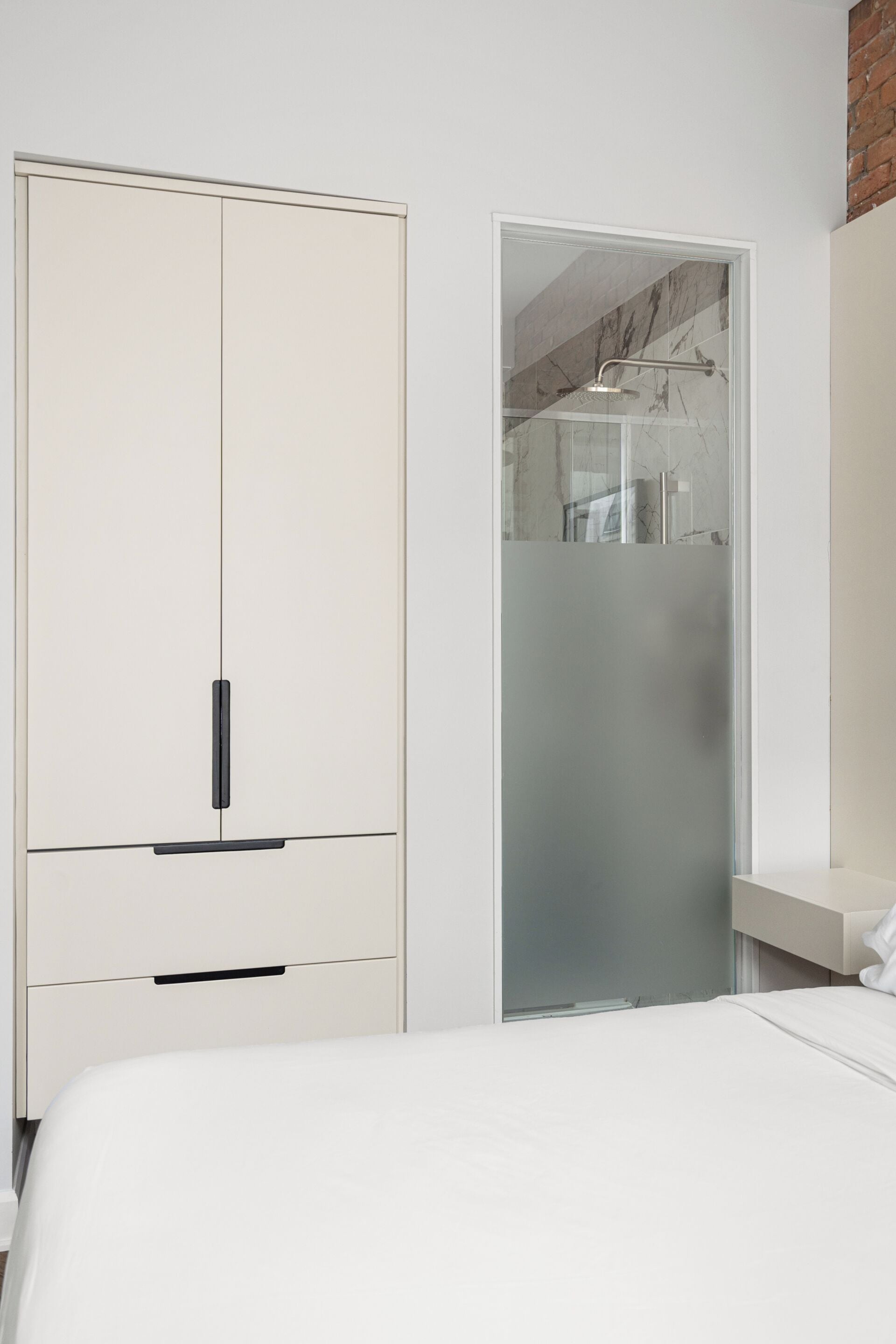 A bedroom with a bed, a wardrobe, and a shower area.