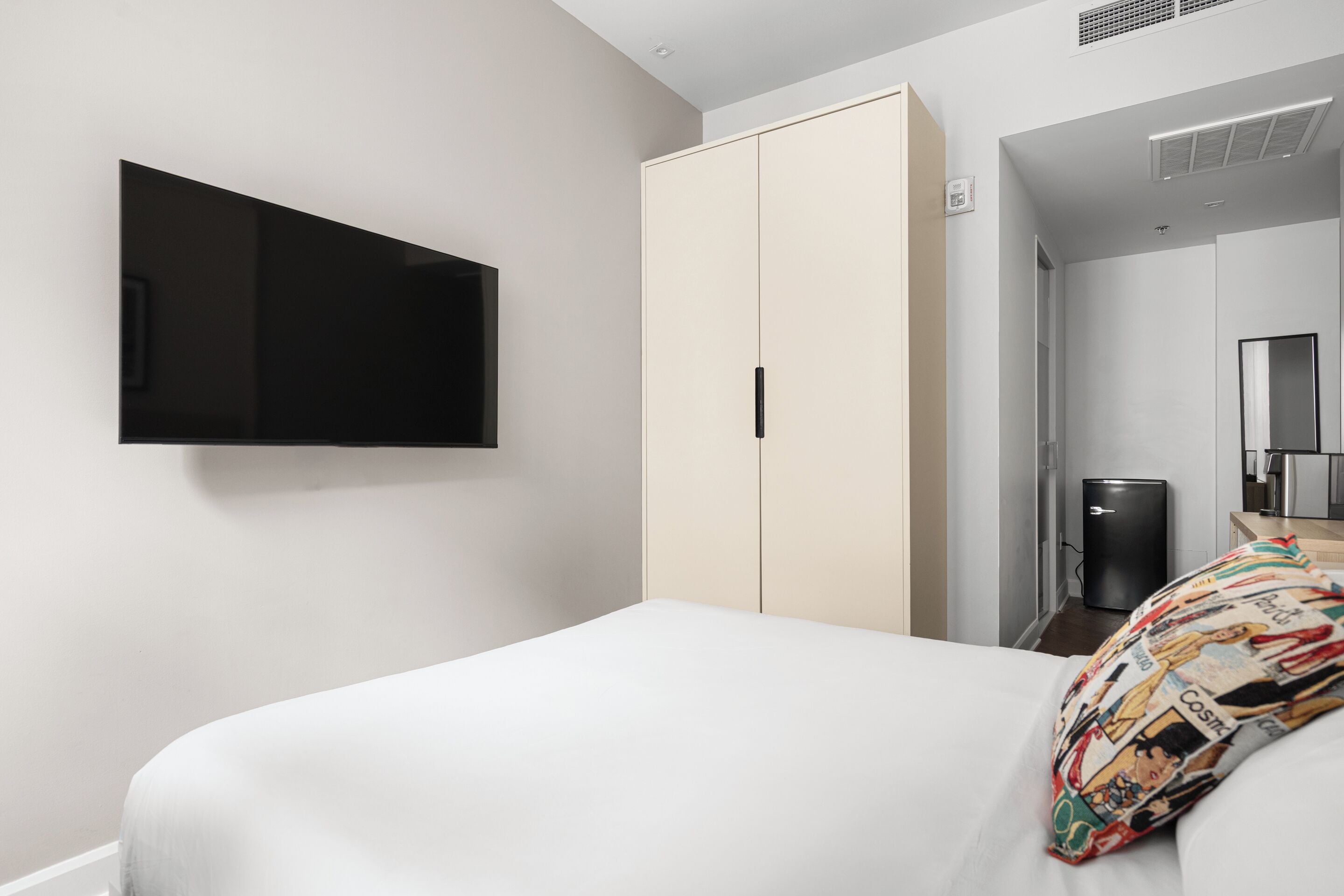 Une chambre d’hôtel moderne équipée d’un lit, d’une armoire, d’une télévision et d’un petit réfrigérateur.