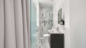 A modern bathroom with a marble floor, a white toilet, a dark vanity, and a glass shower enclosure.