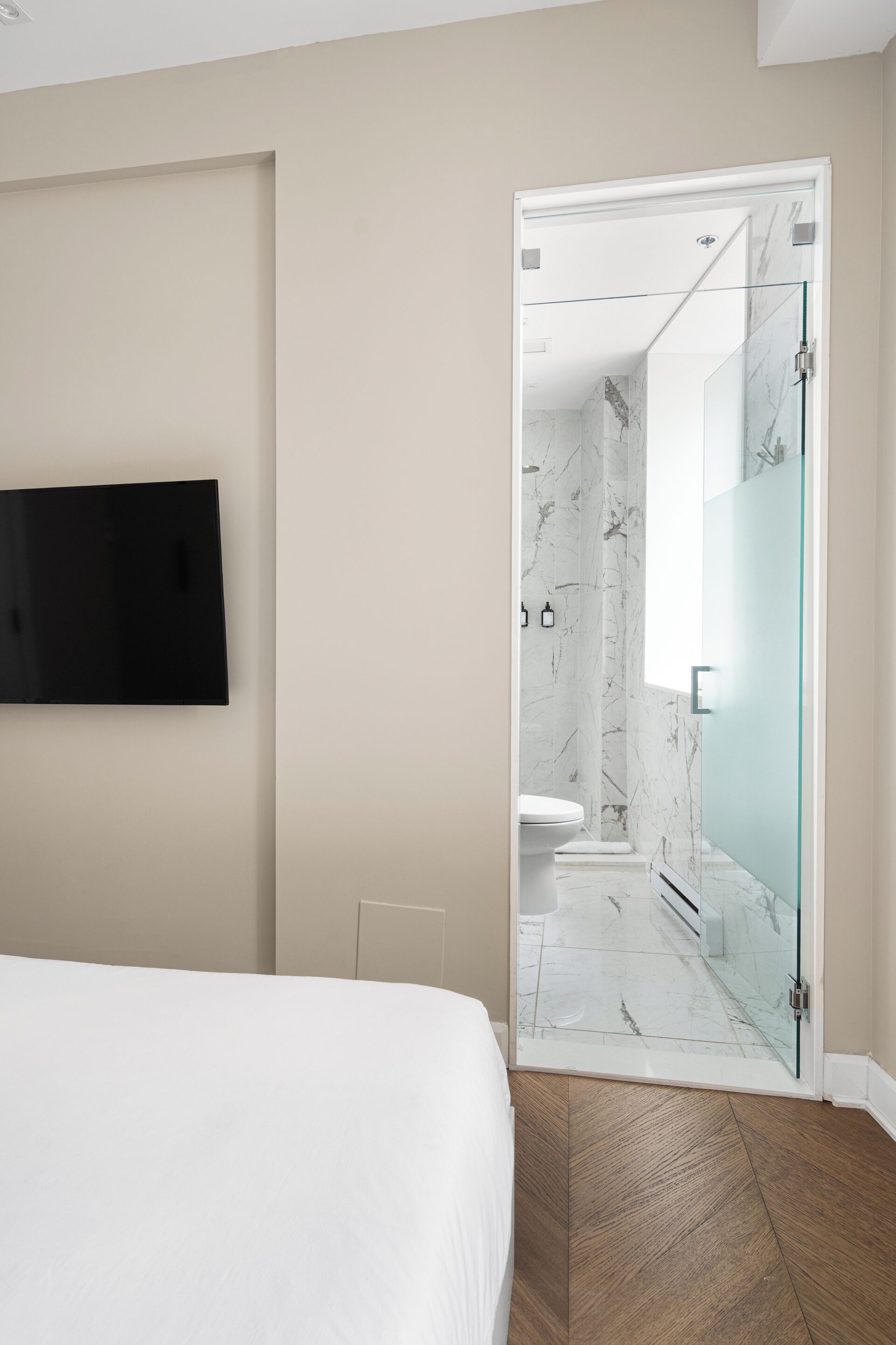 A modern bathroom with a glass shower door, a marble shower wall, and a toilet.