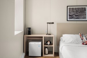 Une chambre d’hôtel compacte comprenant un lit, une petite kitchenette, une machine à café et une œuvre d’art encadrée au mur.