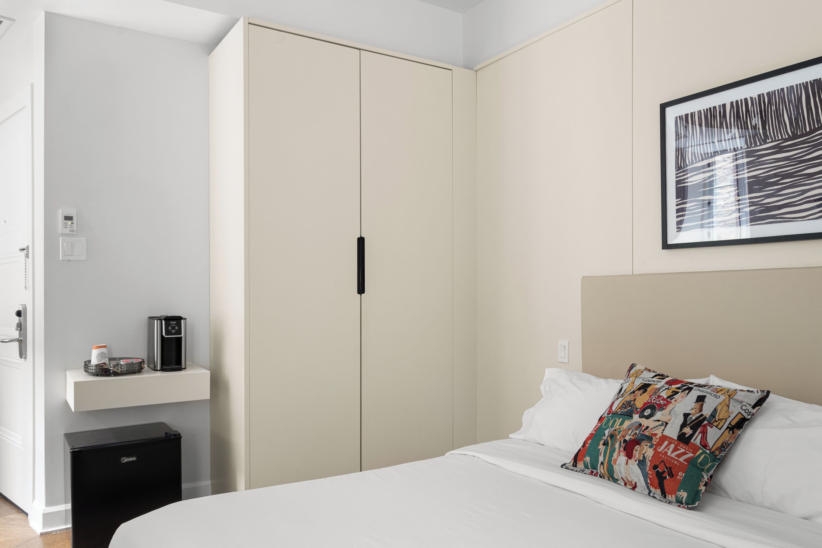 Una camera d'albergo con un letto, una macchina per il caffè, un piccolo armadietto e un guardaroba.