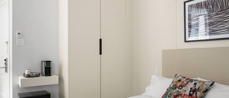 Una camera d'albergo con un letto, una macchina per il caffè, un piccolo armadietto e un guardaroba.