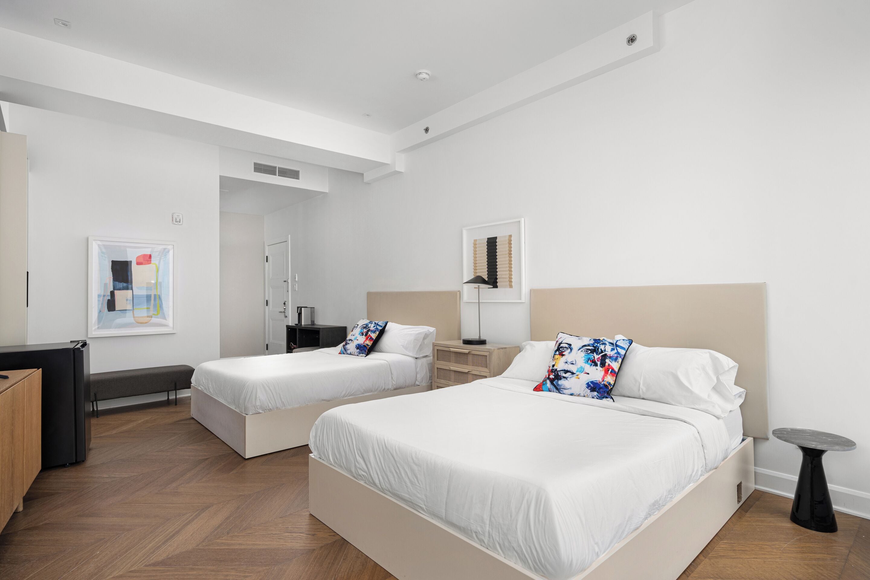 Une chambre d’hôtel moderne équipée de deux lits simples, d’un bureau, d’une chaise et d’une petite table.