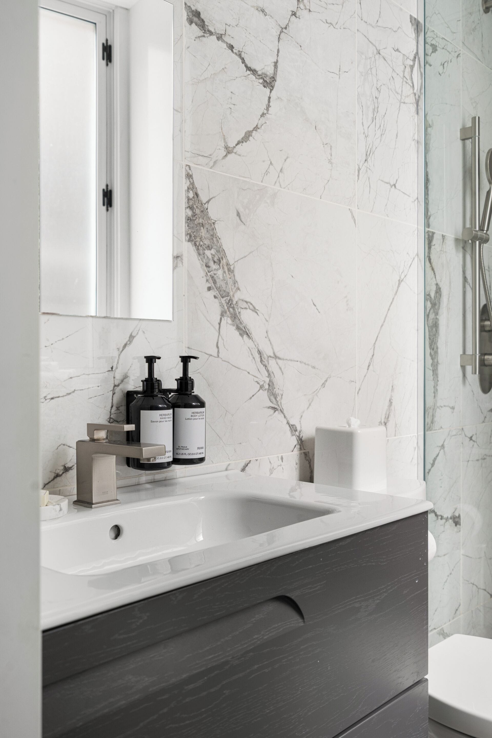 Ein modernes Badezimmer mit Marmor-Spritzschutz, einem weißen Waschbecken und einer dunkelholzfarbenen Waschtischunterschrank.
