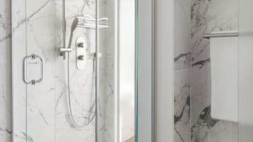 Une douche fermée par des parois en verre, dotée d’un pommeau de douche à main et d’un robinet mural.