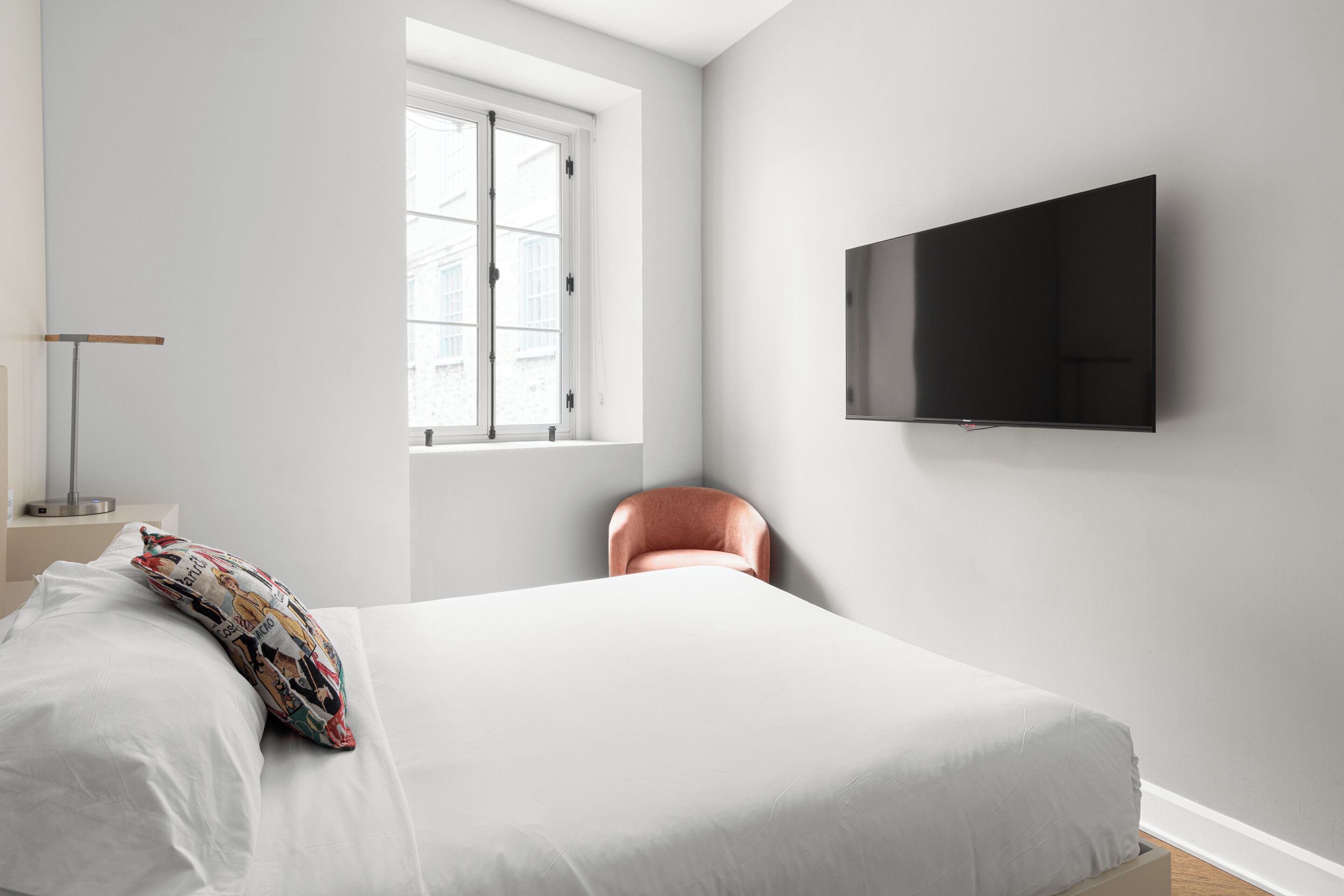 Quarto com cama, televisão na parede, janela e uma cadeira.