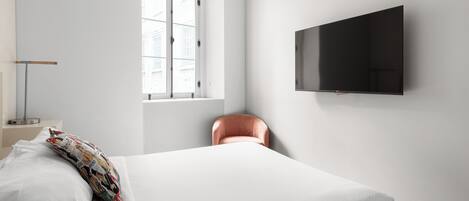 Quarto com cama, televisão na parede, janela e uma cadeira.