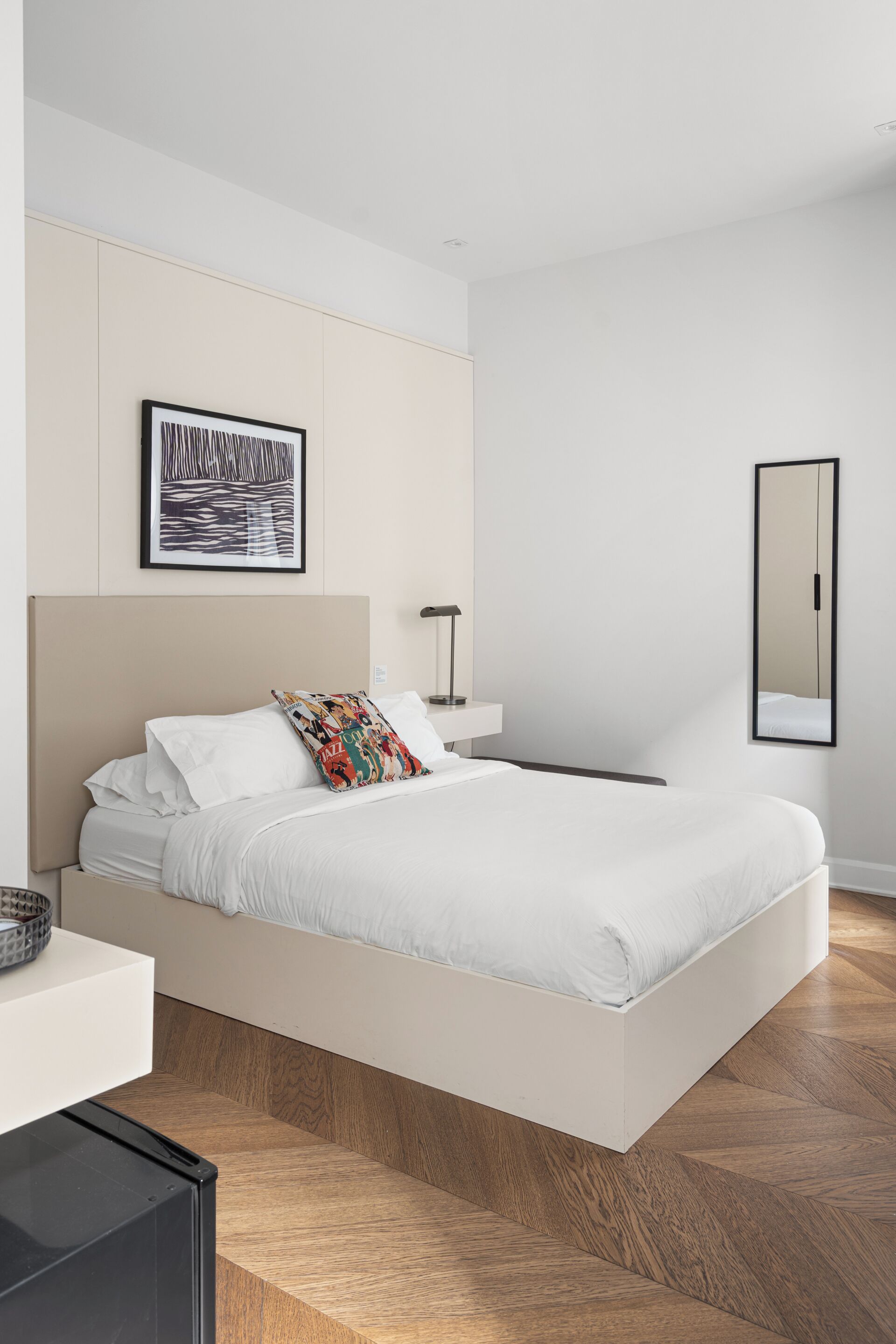 Un dormitorio moderno con una cama grande, una mesita de noche, un espejo y una obra de arte enmarcada en la pared.