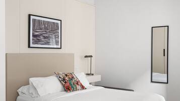 Un dormitorio moderno con una cama grande, una mesita de noche, un espejo y una obra de arte enmarcada en la pared.