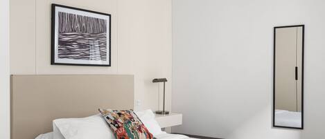 Un dormitorio moderno con una cama grande, una mesita de noche, un espejo y una obra de arte enmarcada en la pared.