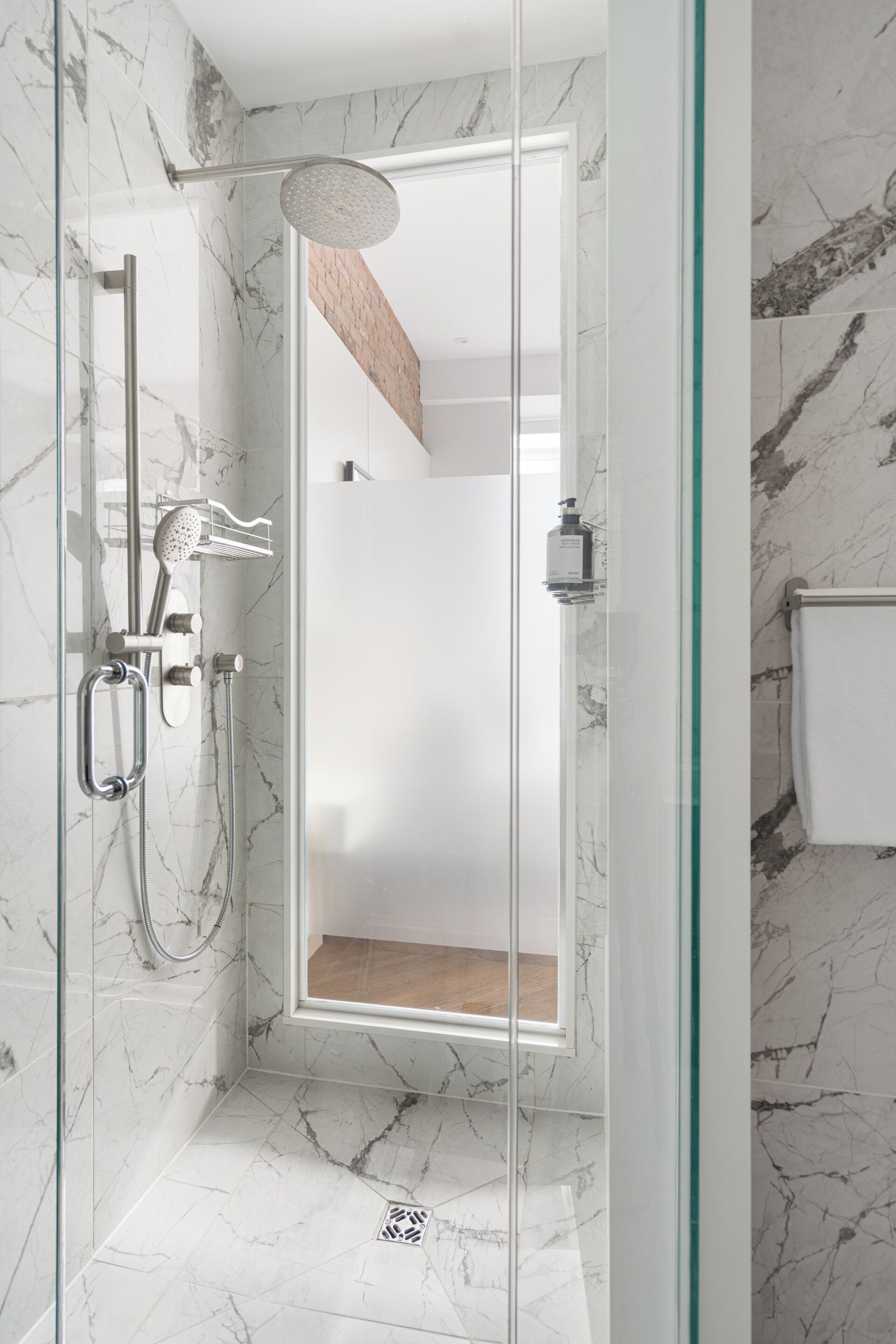 Une douche moderne avec une porte en verre, des murs en marbre et un banc en bois.