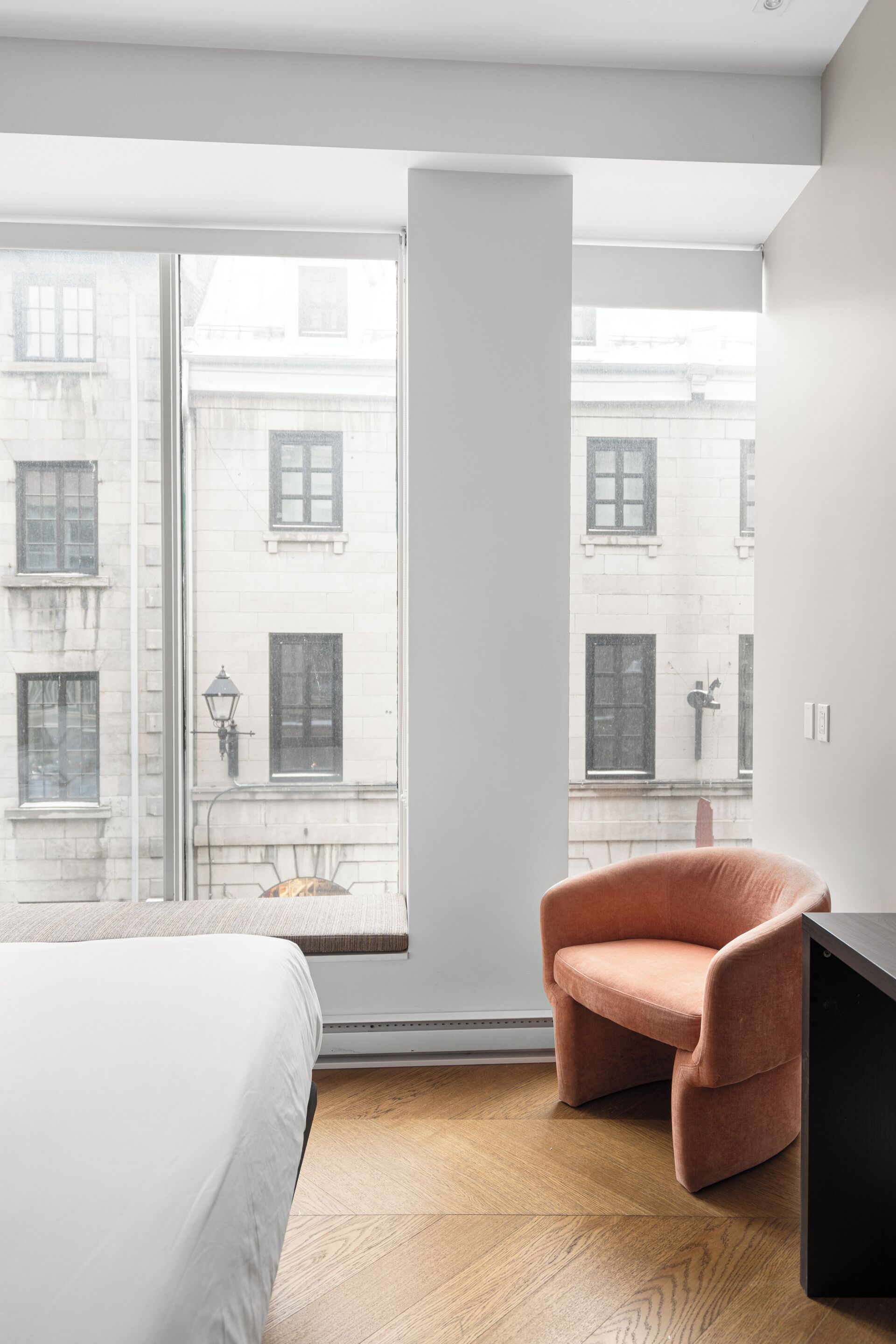 Una camera d'albergo moderna con un'ampia finestra, un letto, una sedia e un tavolino nero.