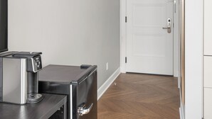 A hallway with a wooden floor, a white door, and a small kitchenette area with a toaster and a refrigerator. - The Bowery Lofts Hotel (Montréal)