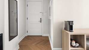 A hallway with a white door, a coffee machine on a wooden shelf, and a framed picture on the wall. - The Bowery Lofts Hotel (Montréal)