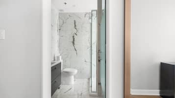 A modern bathroom with a marble wall, a glass shower enclosure, and a wooden floor.