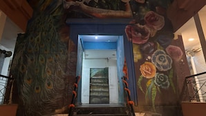 A room with a peacock feather design on the wall, a staircase leading to a door, and a railing with orange decorations. - GoBravo Residences – Kapashera, New Delhi (New Delhi)