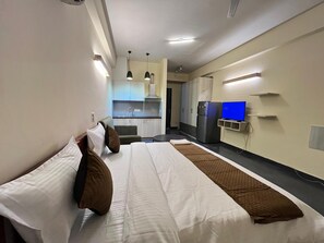 A hotel room with a bed, a small kitchenette, a TV, and a desk. - GoBravo Residences – Kapashera, New Delhi (New Delhi)