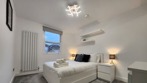 A modern bedroom with a bed, bedside tables, a radiator, a window, and a ceiling light fixture. - Modern 2BR London Apt Near Tube (Greater London)