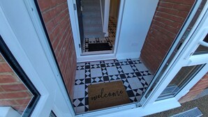 Una puerta con piso a cuadros blanco y negro, un felpudo y una puerta de cristal.