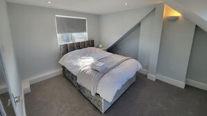 Un dormitorio con una cama grande, una ventana con persianas, una escalera y una lámpara fijada a la pared.