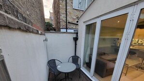 A small outdoor patio with a table and chairs, a sliding glass door leading to an interior space with a sofa and a dining table. - Large 4 Bedroom House In Central London (Greater London)