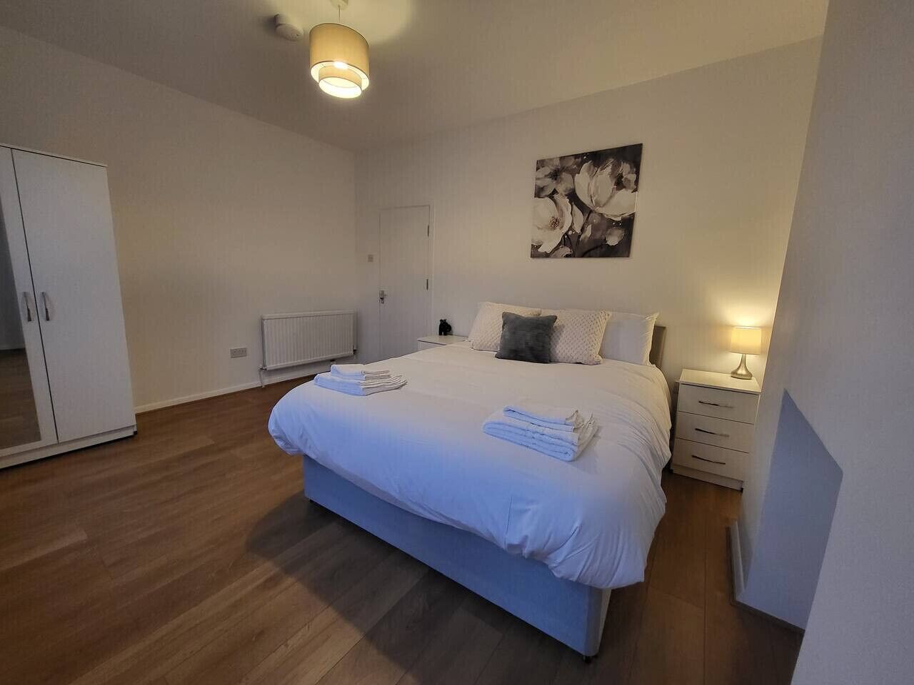 A bedroom with a large bed, a wardrobe, a radiator, and a wall-mounted artwork.