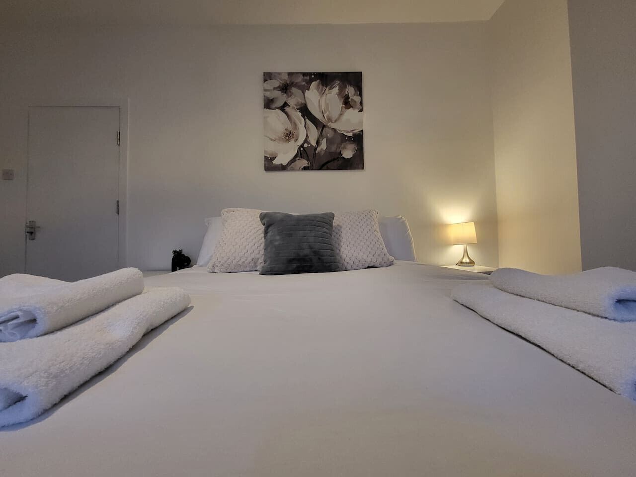 A hotel room with a large bed, two pillows, a nightstand with a lamp, and a painting on the wall.