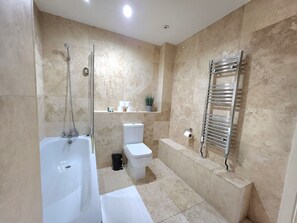 A bathroom with a bathtub, toilet, and a towel rack. - Spacious 2-Bed Flat - Close to Tube, Sleeps 6 (Greater London)