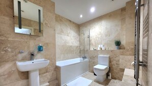 Et moderne badeværelse med vask, badekar, toilet og bruser.