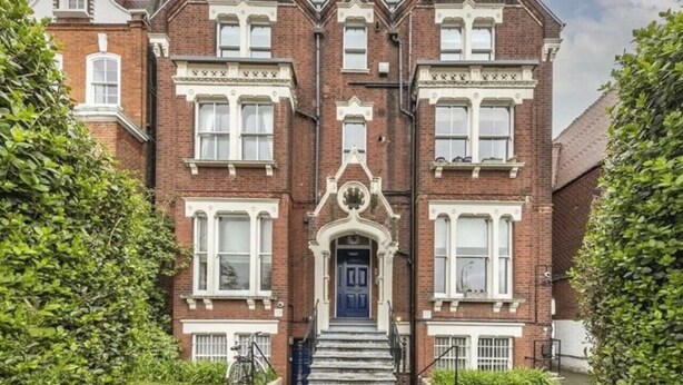 Un edificio de ladrillo de dos pisos con una entrada central, varias ventanas y una escalera que lleva a la puerta principal.