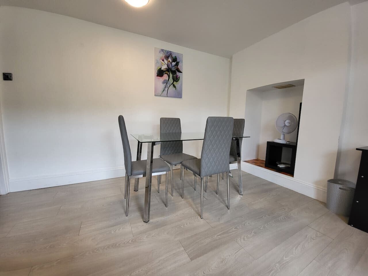 A dining area with a glass table and four grey upholstered chairs.