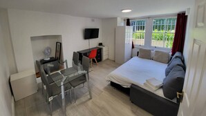 Un dormitorio moderno con cama, escritorio, silla, televisor y ventana con cortinas.