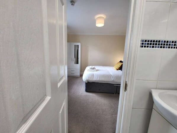 A narrow hallway leading to a bedroom with a bed, a wardrobe, and a bathroom with a sink.