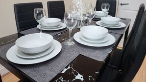 A dining table set with white plates, bowls, and wine glasses, surrounded by black chairs. - Tooting Bec Central Apartment by London Tube (Tooting Bec, London)