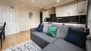 A modern living room with a grey sofa, patterned rug, and a dining area with a white door and black chairs. - Tooting Bec Central Apartment by London Tube (Tooting Bec, London)