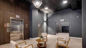 Eine moderne Lobby mit Aufzug, einer Rezeption und einem Wartebereich mit Stühlen und einem Tisch.