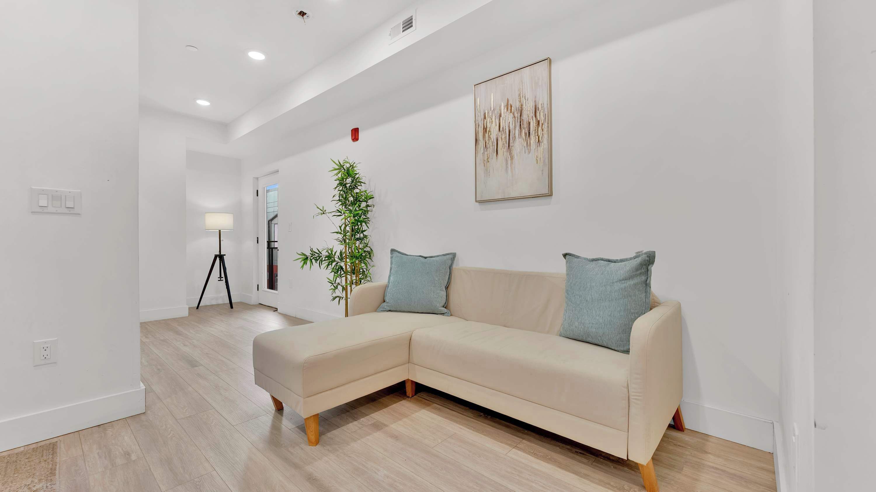 Un salon moderne avec un canapé d’angle beige, un lampadaire et un grand tableau abstrait accroché au mur.