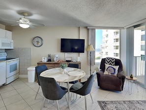 Un salon moderne avec une table à manger ronde, deux chaises, un canapé, un téléviseur et un balcon offrant une vue sur les immebles.