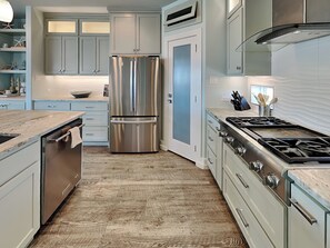 A modern kitchen with a stainless steel refrigerator, a gas stove, and light blue cabinets. - Salty Kisses | Private Pool, Ocean Views (Corpus Christi)