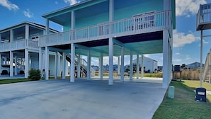 Una casa moderna frente a la playa con un porche cubierto, varios balcones y un amplio espacio exterior.