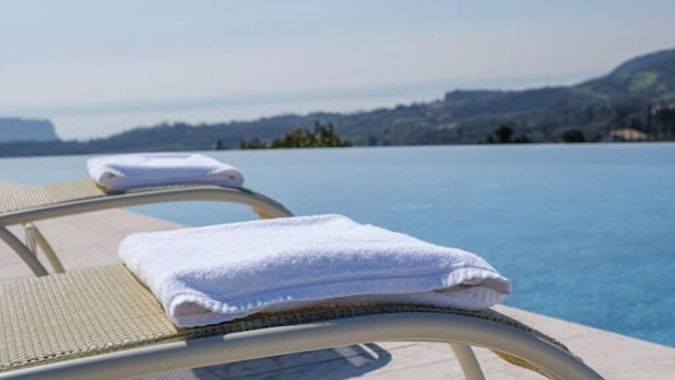 Une chaise longue installée au bord de la piscine, avec une serviette blanche, d’où l’on peut admirer un plan d’eau paisible et des collines lointaines.