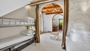 Une chambre de dortoir avec des lits superposés, un plafond en bois et une porte en arc donnant sur un espace repas.