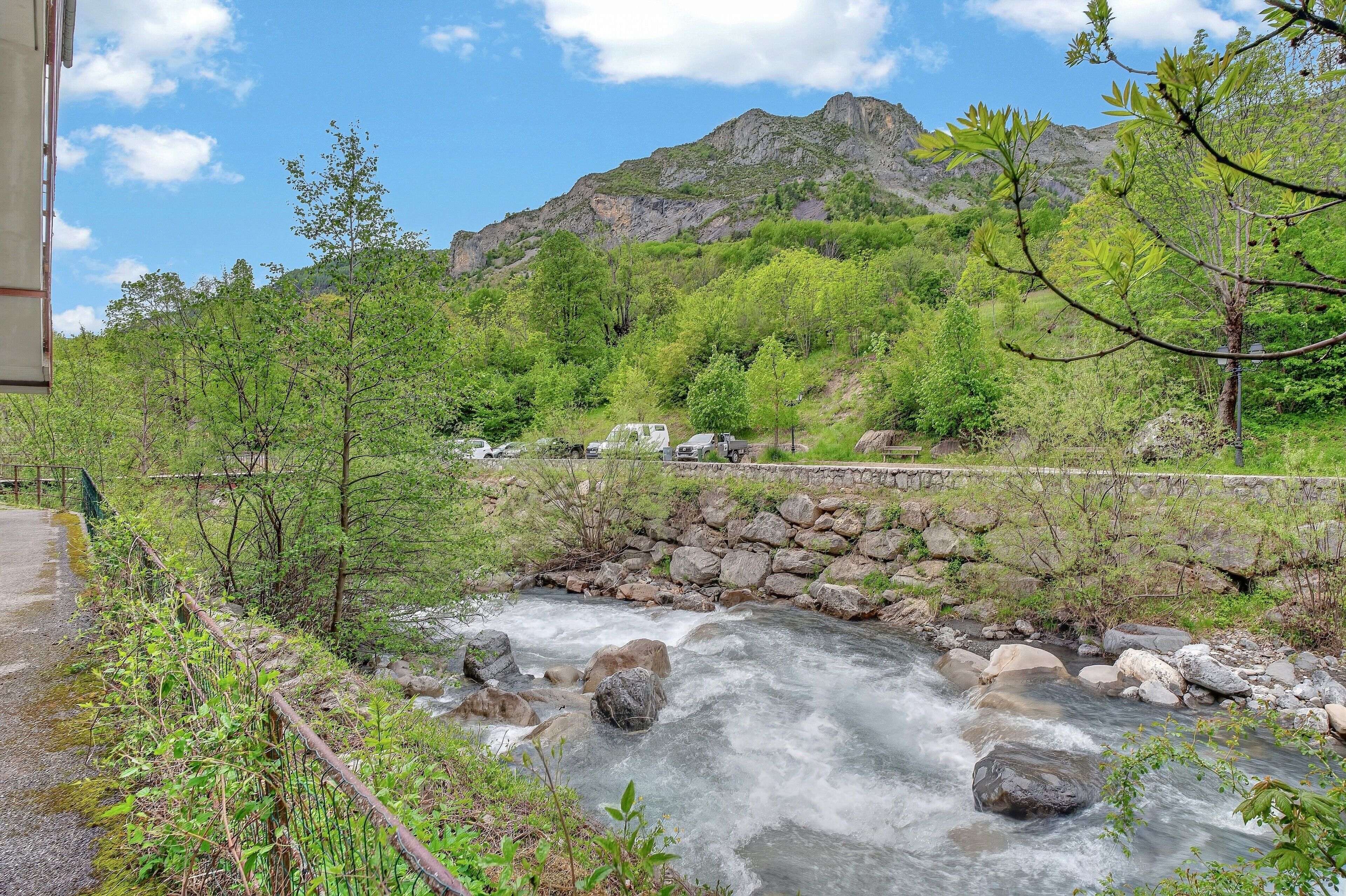 Un río serpentea por una zona montañosa con un muro de piedra y una carretera.