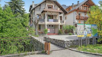 Ein traditionelles Chalet mit Steinaußenwand, hölzernen Balkonen und freiem Blick auf die umliegende Grünfläche.