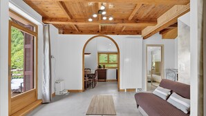 Une pièce avec un plafond en bois, un canapé, une table et une vue sur une cuisine et un jardin, visibles à travers une arche.
