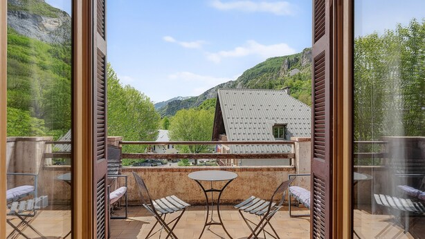 Un balcon avec une table et des chaises, donnant sur un paysage montagneux.