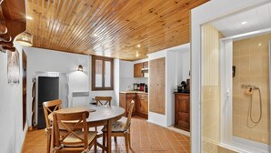 Una cocina con armarios de madera, una mesa de comedor con sillas y un área de ducha con puerta de vidrio.