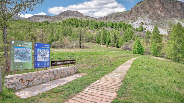 Un sendero de piedra que lleva a una zona montañosa, con señalización que indica los senderos 'ESPACE PROMENADE' y 'ESPACE NORDIQUE'.