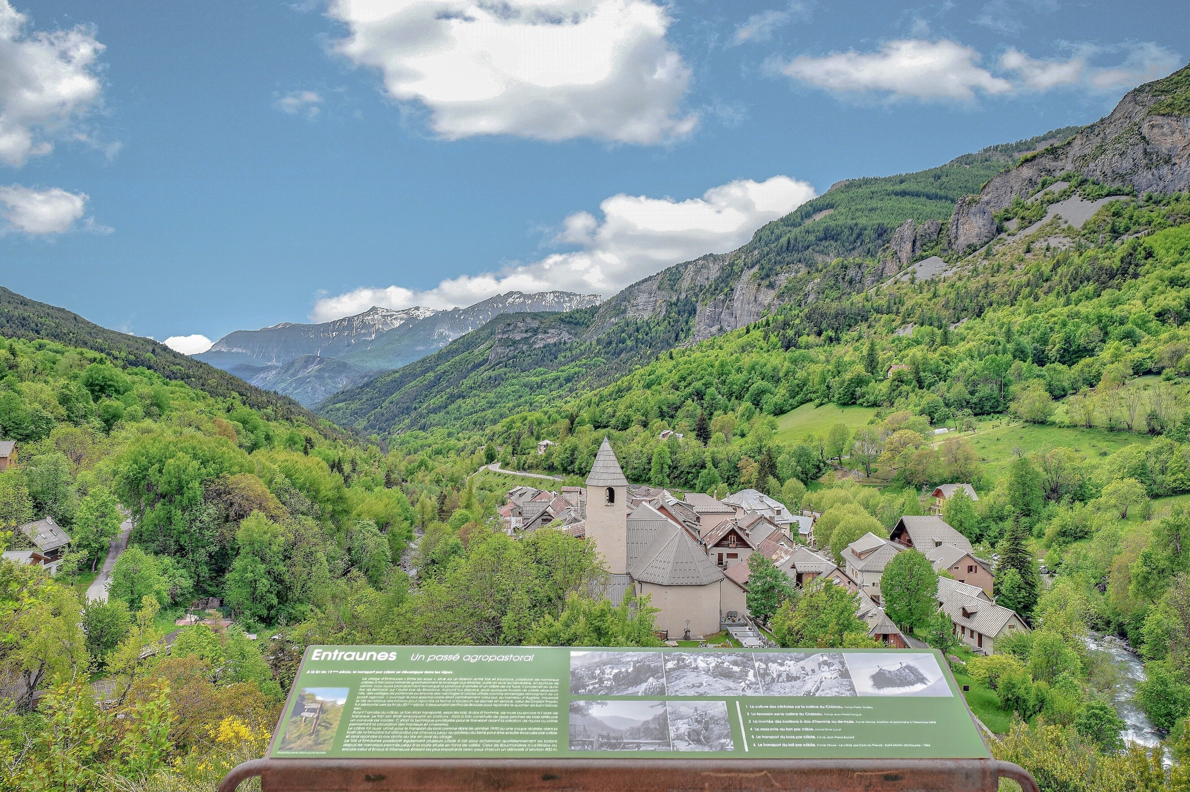 Un pueblo de montaña con una iglesia, rodeado de abundante vegetación y un cielo despejado.